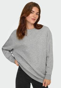 Sudadera gris con escote redondo, hombros caídos y puños acanalados. La tela parece suave con una textura sutil.