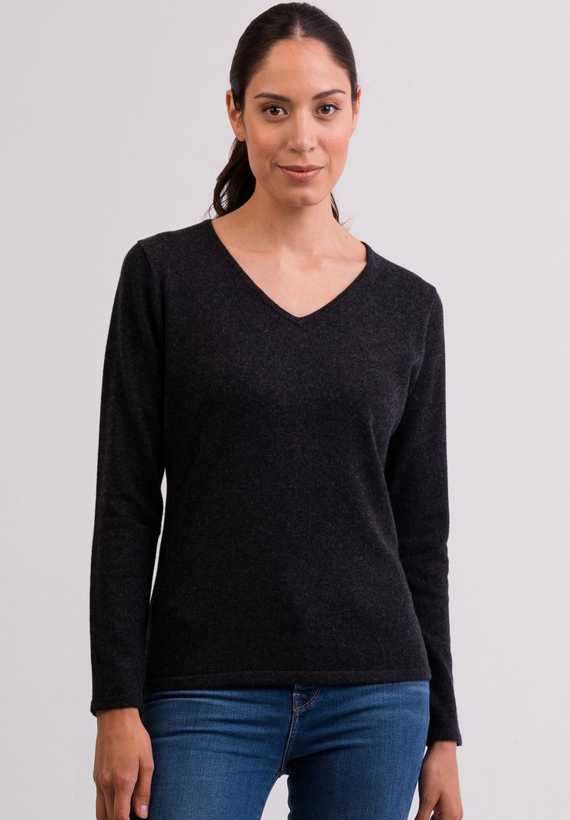 Maglione nero a maniche lunghe realizzato in tessuto testurizzato con scollatura a V. Abbinato a jeans blu, che evidenziano una silhouette aderente.