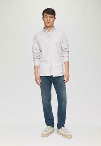 Lichtpaars gestreept overhemd met knopen, blauwe jeans en witte sneakers met beige accenten. Casual fit, lange mouwen en zichtbare stiksels.