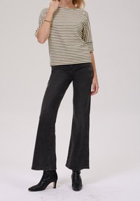 Gestreiftes creme- und schwarzes Kurzarmoberteil, kombiniert mit hochgeschnittenen schwarzen Schlagjeans und spitzen schwarzen Ankle Boots. Minimalistisches Design.