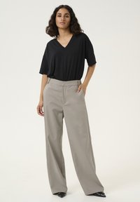T-shirt noir à col en V associé à un pantalon large gris clair, avec une texture de tissu lisse et une coupe décontractée. Des chaussures noires pointues complètent la tenue.