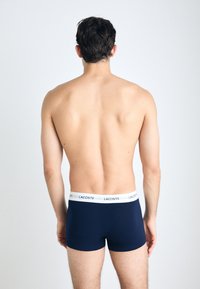 Marineblauwe boxershorts van gladde stof met een witte tailleband waarin het "LACOSTE" logo is verwerkt. Eenvoudig ontwerp, zonder patronen of accenten.