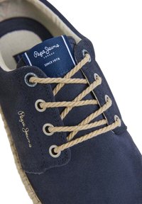 Zapato de ante azul marino con cordones beige, con puntera redonda y suela trenzada. Una etiqueta azul muestra "Pepe Jeans London" y el año de establecimiento.