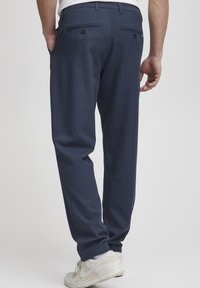 Navy blue tailored pants with a smooth texture, slim fit, rear pockets, and a clean design. Paired with white sneakers.