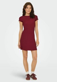 Robe bordeaux à manches courtes avec un corsage ajusté et un ourlet évasé. Tissu doux et texturé avec un motif en côtes subtil. Portée avec des chaussures décontractées.