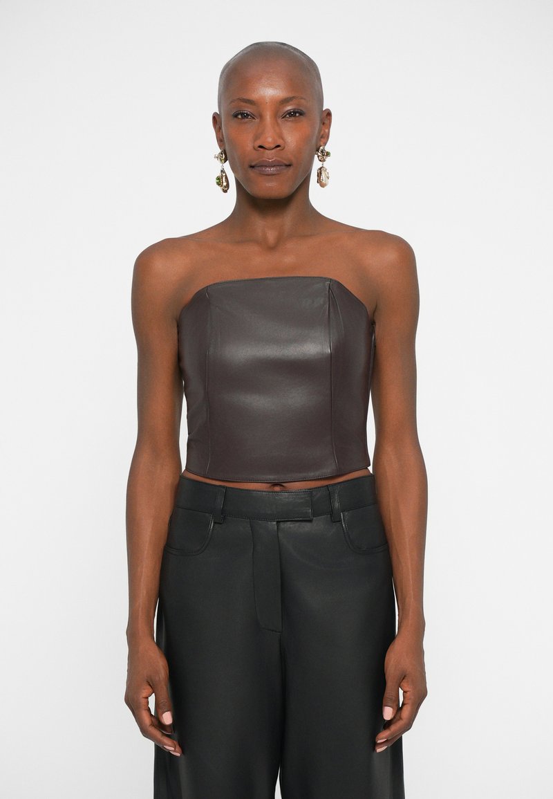 Bruine leren strapless crop top met een gestructureerd ontwerp, gecombineerd met hoge zwarte broeken, met gladde texturen en strakke lijnen.