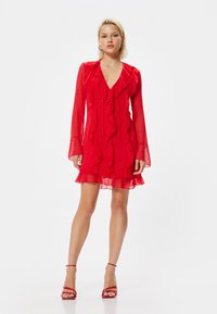 Rotes Chiffonkleid mit durchsichtigen langen Ärmeln, gerafftem Ausschnitt und Saum, das einen taillierten Oberteil und einen ausladenden Rock mit dezenten Punkten aufweist.