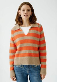 Gestreifeter Pullover in Orange und Beige, mit V-Ausschnitt und Kragen-Design. Gerippter Saum und Bündchen mit weicher Textur. Über einem weißen Oberteil getragen.