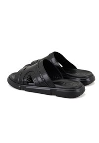 Zwarte synthetische slippers met een gestructureerde bovenkant met horizontale en diagonale uitsparingen. Dikke zool met een subtiel geometrisch patroon.