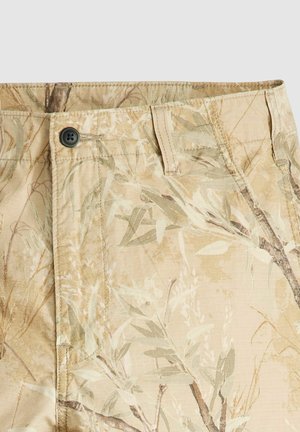 Pantalones cortos de tela beige con un estampado botánico. Presentan un cierre de botón y costuras visibles. El material tiene un aspecto ligero y texturizado.