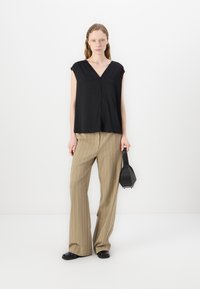 Top nero a maniche corte con scollo a V, abbinato a pantaloni beige a righe e una piccola borsa nera. Tessuto morbido, vestibilità rilassata.