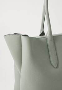 Zelena usnjena torba za čez ramo z minimalističnim dizajnom, ki ima gladko teksturo, trdne ročaje in čiste šive ob robovih.