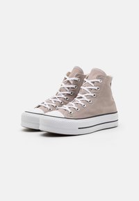 Beige canvas high-top sneakers with white laces, rubber toe cap, and thick white sole with black stripe detailing.