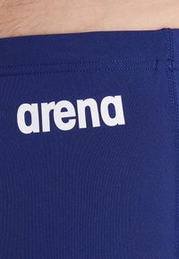 Marineblaue Badehose mit glatter Textur. Mit einem weißen "arena"-Logo am Bund und verstärkten Nähten entlang der Kanten.