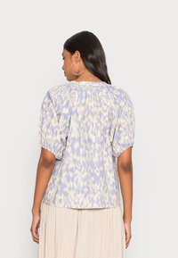 Blusa de manga curta em azul claro com padrão abstrato amarelo, apresentando um decote franzido e mangas bufantes. Textura de tecido macio.