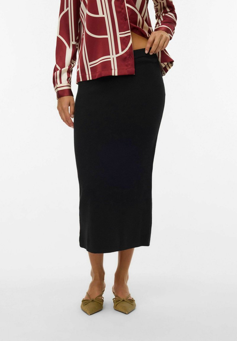 Falda midi negra de suave tejido, de forma ajustada, combinada con una blusa de patrón geométrico en color burdeos y blanco, complementada con zapatos planos en color oliva.