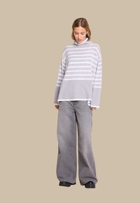 Grå stripete halsen sweater med løs passform, paret med grå vide jeans. Glatt tekstur og kontrasterende striper gir visuell interesse.