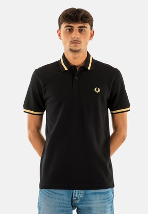 Camisa polo negra de algodón, con acentos amarillos en el collar y las mangas, y un pequeño logotipo dorado en el pecho.