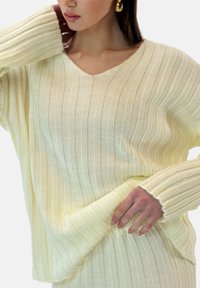 Lys beige strikket sweater med lodrette ribbinger, V-hals og lange ærmer med rå kanter. Blød tekstur med en afslappet pasform.