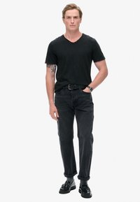 Sort v-hals t-shirt, mørkegrå jeans, sorte sko. Funktioner inkluderer optrullede ærmer, en glat stofstruktur og et minimalistisk design.