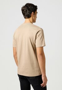 Beige puuvillapaita lyhythihaisilla ja pyöreällä kaula-aukoilla, jossa on sileä pinta ja minimaalinen ommeltyyli.