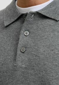 Pogled izbliza na sivi pleteni polo majicu s preklopljenim ovratnikom, sa dva tamna dugmeta zakopčana, koja se nosi preko bijele majice s okruglim izrezom.