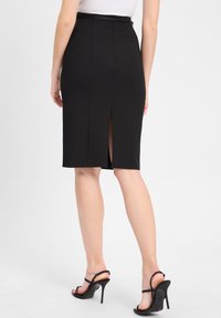 Schwarzer Bleistiftrock aus eng anliegendem Material, mit einem Rückenschlitz und dezenten Nahtdetails, kombiniert mit schwarzen Riemchen-High Heels.