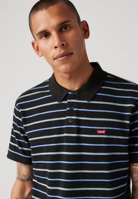 Black polo shirt with horizontal blue and gray stripes. Features a button placket, black collar, and a red Levi's logo on the chest.