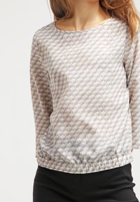 Blouse légère à motifs dans des tons crème et taupe. Dotée d'un col rond, de manches trois-quarts et de détails froncés à la taille.