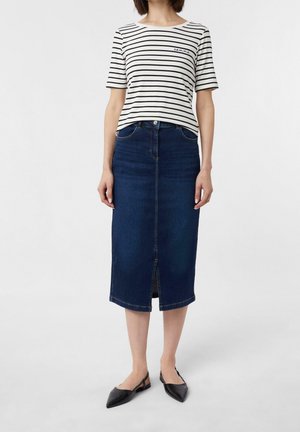 Femme portant un t-shirt à manches courtes rayé noir et blanc, une jupe en jean bleu foncé longueur genou avec une fente devant, et des ballerines noires pointues.