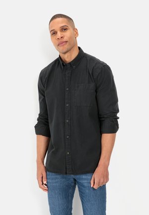 Black button-up shirt with a single chest pocket, rolled sleeves, and a slightly textured fabric. Paired with blue denim jeans.