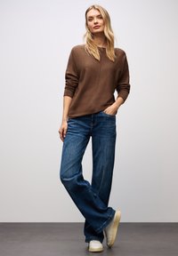 Maglione lavorato a maglia marrone con scollatura rotonda e maniche lunghe, abbinato a jeans blu a gamba larga e sneaker bianche. Un look semplice e informale.