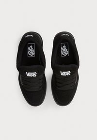 Paire de baskets Vans noires avec le logo Vans blanc sur les languettes et les semelles intérieures, vues de dessus sur un fond clair uni.