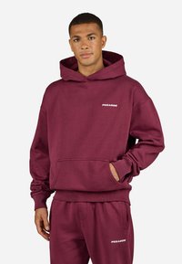Maroon cotton hoodie with a front pocket and ribbed cuffs, featuring a white "PEGADOR" text logo on the chest.