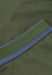 Olivově zelená látka s hladkým povrchem, která má modro-zelenou elastickou gumu s vyšívaným nápisem "intimissimi" v modré barvě.