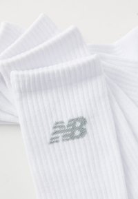 Trois paires de chaussettes blanches à côtes avec un logo "NB" gris, soigneusement disposées sur un fond clair.