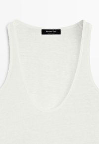 Haut blanc sans manches à col en V avec étiquette de la marque Massimo Dutti cousue à l'intérieur du col, fabriqué au Cambodge.