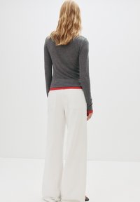 Top gri cu mânecă lungă, cu tiv roșu, asortat cu pantaloni largi albi. Spatele are un design ajustat, cu două buzunare la spate.