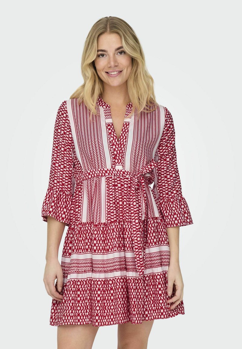 Robe rouge à motifs avec des manches longues, des poignets volantés, une taille ceinturée et une jupe à étages présentant des motifs géométriques et des rayures alternés.