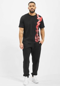 Black t-shirt featuring bold red text "DANGEROUS" on the left side, paired with black sweatpants and white sneakers.