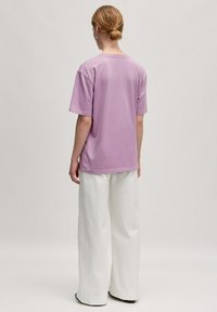 Lichtpaarse oversized t-shirt met korte mouwen, ronde hals, gecombineerd met ruime witte broek, gladde stof, minimalistisch ontwerp.
