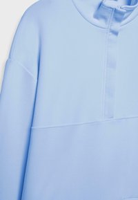 Jasnoniebieski sweter z długimi rękawami, wysokim kołnierzem i częściowym zapięciem na przodzie.