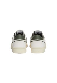 Zapatillas blancas con acentos verdes, parte superior de cuero suave, punta redondeada, collar acolchado y suela de goma texturizada. Logo de la marca en el talón.