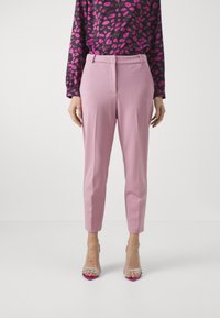 Light pink tapered trousers with a smooth texture, featuring a front crease and side pockets, paired with clear high-heeled sandals.