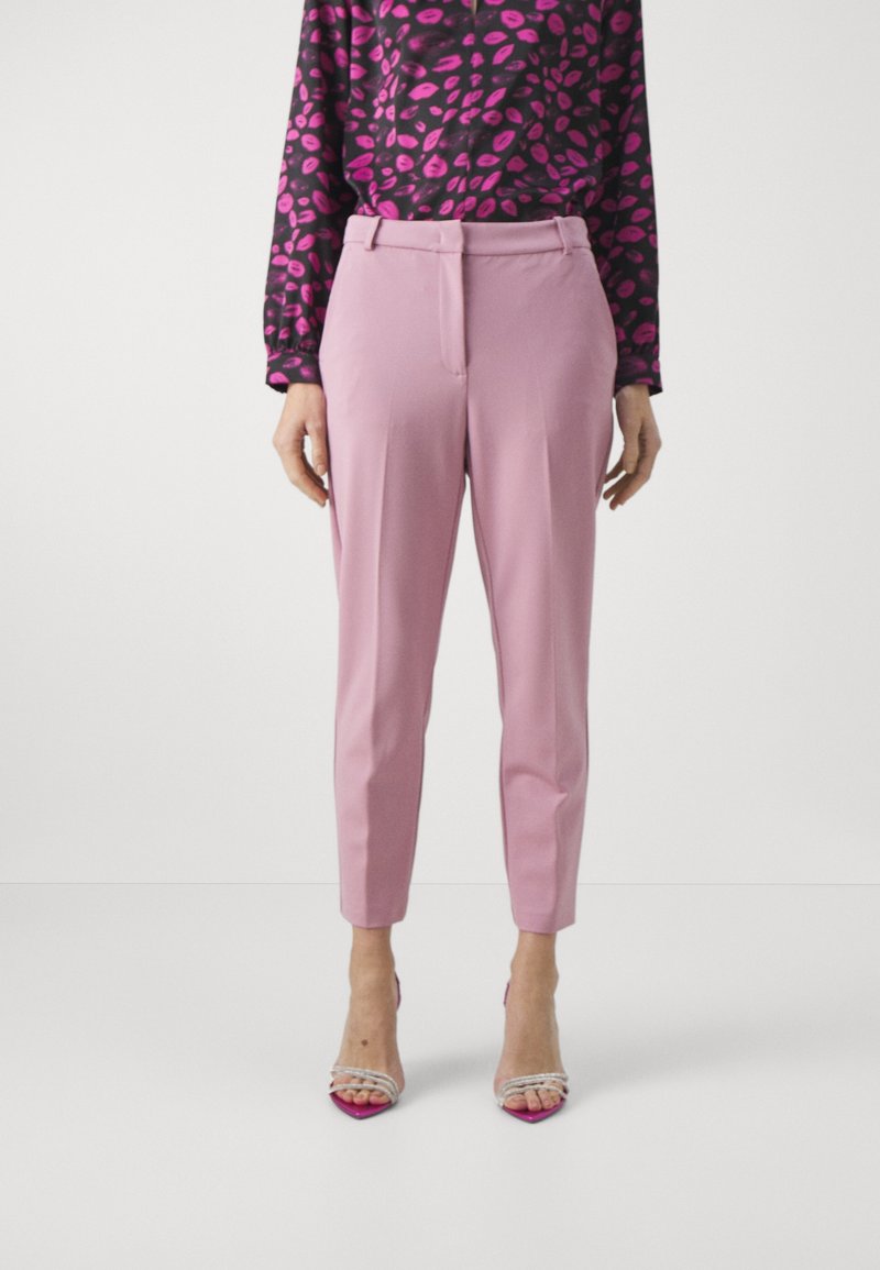 Light pink tapered trousers with a smooth texture, featuring a front crease and side pockets, paired with clear high-heeled sandals.