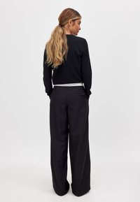 Schwarzer, kurzes Sweatshirt und schwarze, weit geschnittene Hose. Das Sweatshirt hat einen runden Ausschnitt; die Hose verfügt über Gesäßtaschen und hat eine glatte Textur.