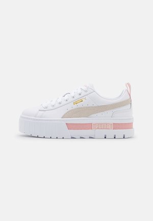 Biały sneaker Puma z grubą podeszwą, beżowym paskiem, różowym akcentem na śródpodeszwie, złotym logo z boku i różową pętlą na pięcie na jednolitym tle.