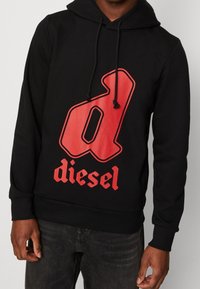 Svart hoodie med en stor röd "d"-logotyp och ordet "diesel" i rött. Har en justerbar huva och ribbade muddar vid ärmarna och midjan.