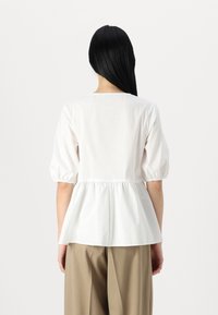 Bílý peplum top s nabíranými rukávy, hladká bavlněná tkanina, nabraný pas a kulatý výstřih, doplněný béžovými kalhotami.