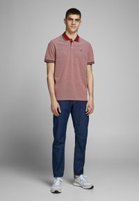 Rode gepaspelde polo met een contrasterende marineblauwe en witte kraag, gecombineerd met blauwe spijkerbroeken en grijze sneakers. Opvallend geborduurd logo op de borst.